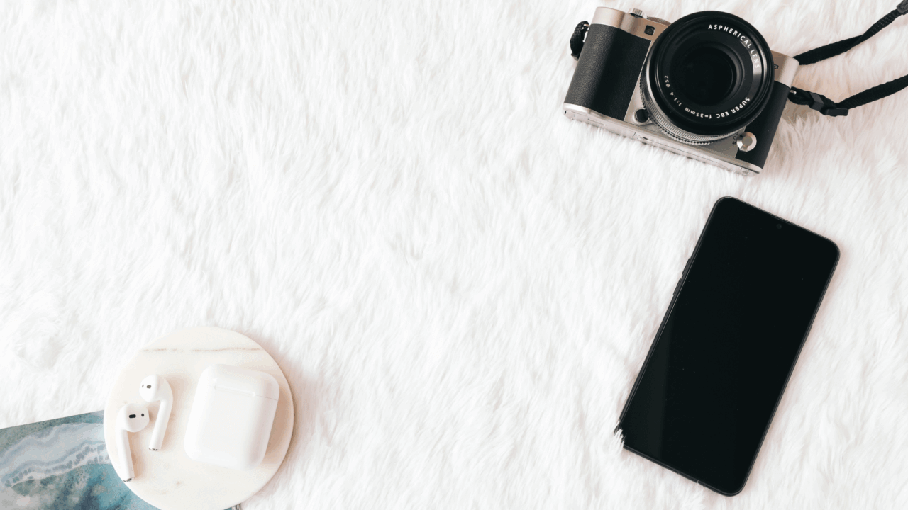 Flatlay with camera, smartphone and earbuds on white background—tools for wedding PR outreach and wedding publicity pitching